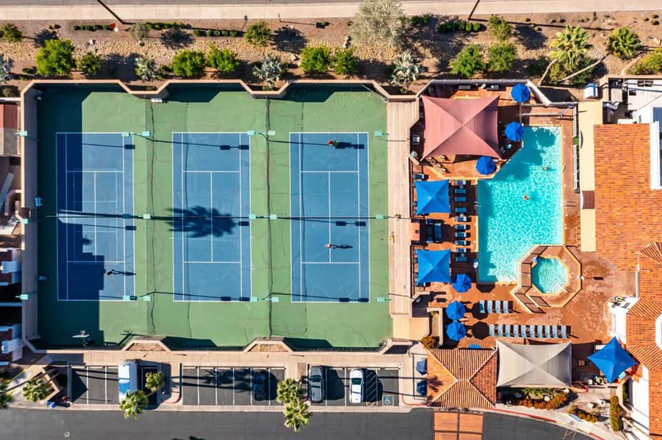 Aerial view of resort with three tennis courts, turquoise pool, and blue umbrellas on terracotta deck
