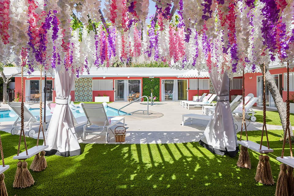 Outdoor garden venue with hanging purple and pink wisteria flowers, lounge chairs, and pool area