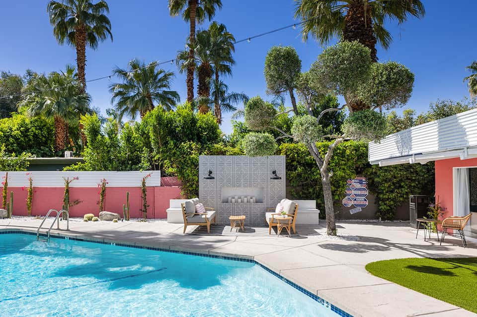 Resort pool area with lounge chairs, palm trees, fireplace feature wall, and clear blue water