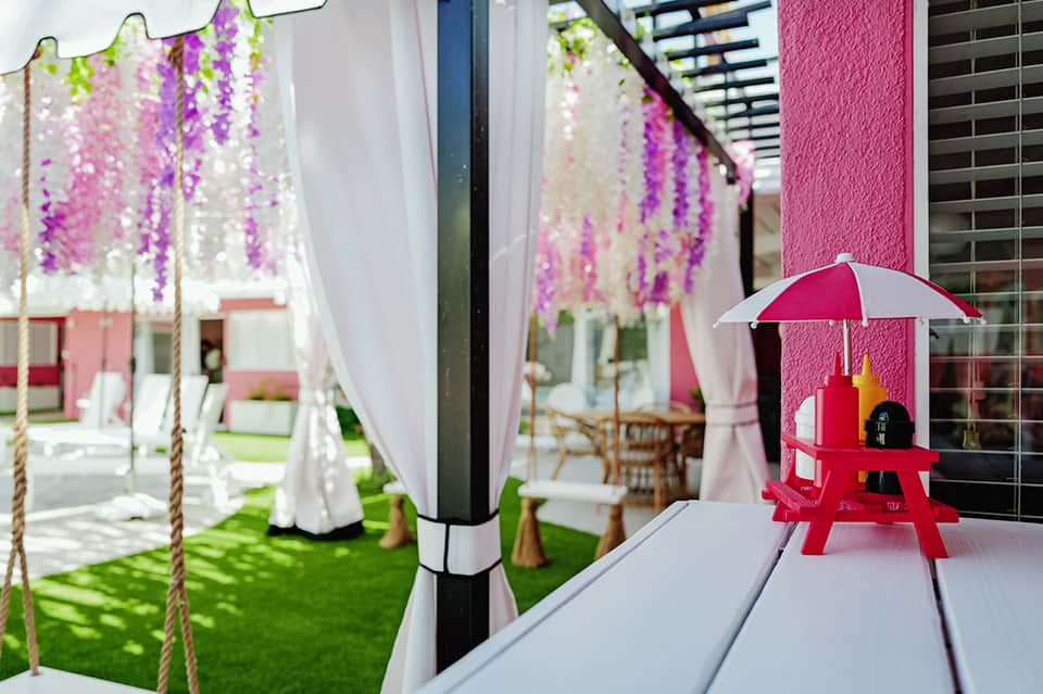 Outdoor garden venue with hanging purple flowers, white drapes, and red picnic table