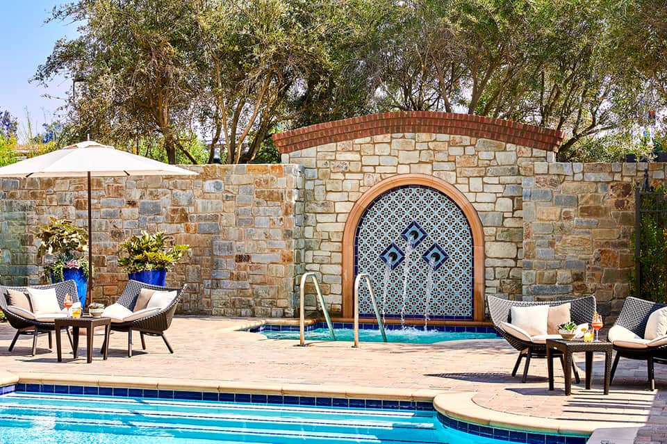 Spa area with decorative stone wall, Moroccan-style archway, lounge chairs, and umbrella by small pool