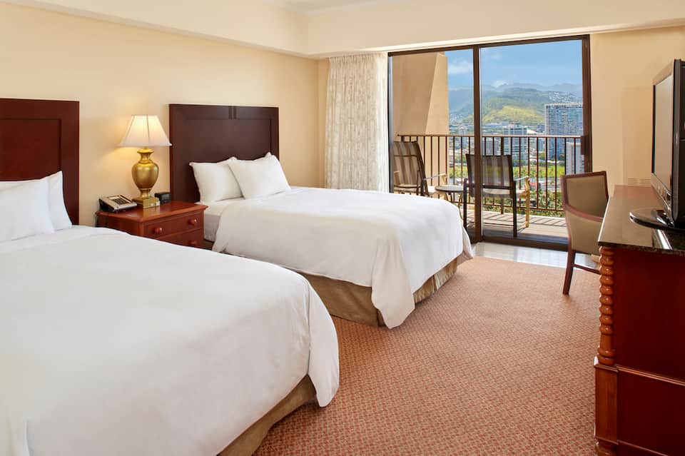 Hotel bedroom with two queen beds, balcony overlooking mountains and cityscape