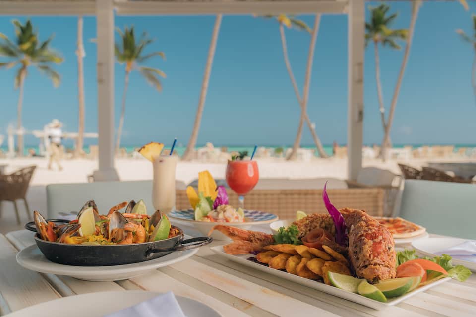 Beachfront restaurant with seafood dishes, tropical cocktails, and ocean view through palm trees