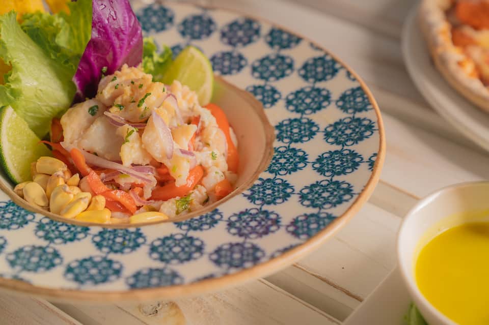 Plated ceviche dish with shrimp, colorful vegetables, and lime on patterned plate