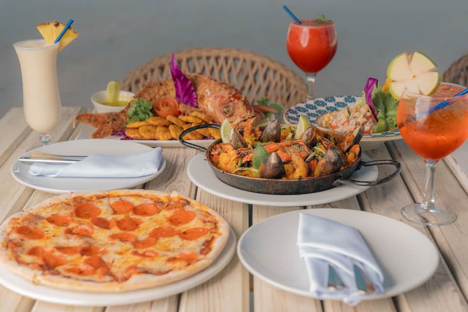 Upscale outdoor dining spread with pizza, grilled seafood, colorful cocktails, and appetizers