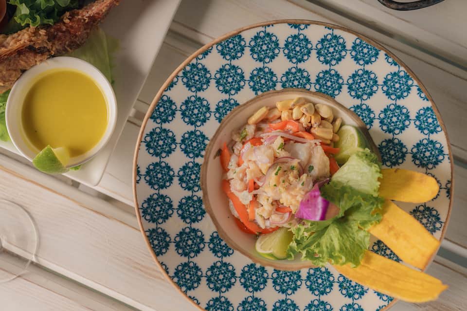 Plated seafood ceviche appetizer with mango, lettuce, and lime on decorative blue plate