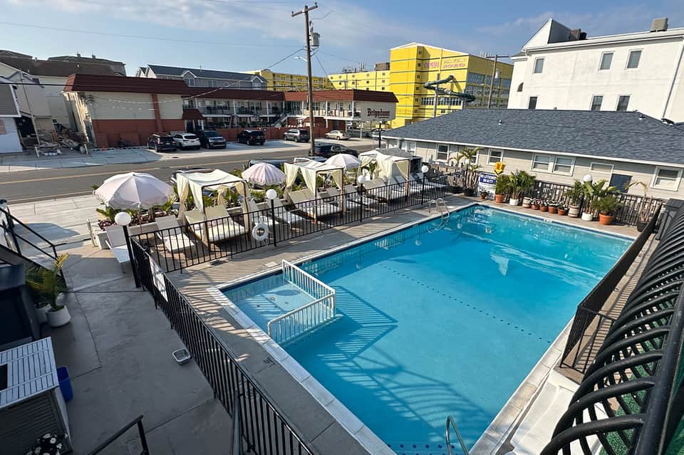 Rooftop pool with blue water, white umbrellas, cabanas, and urban cityscape in background