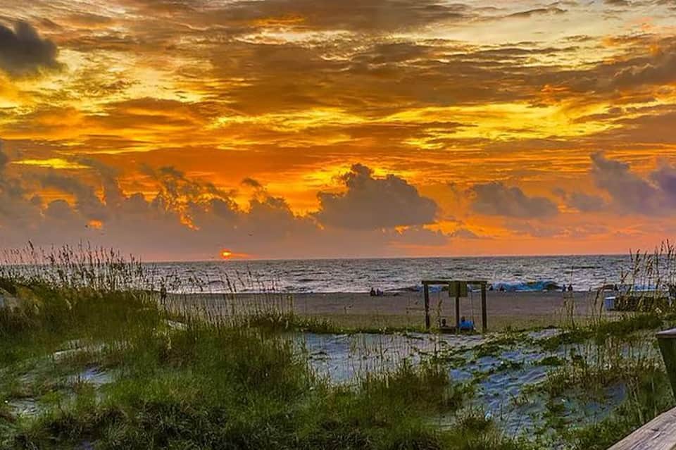 Dramatic sunset over ocean beach with golden clouds and grassy dunes at evening