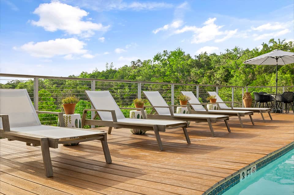 Resort pool deck with wooden loungers, umbrella, and lush forest views