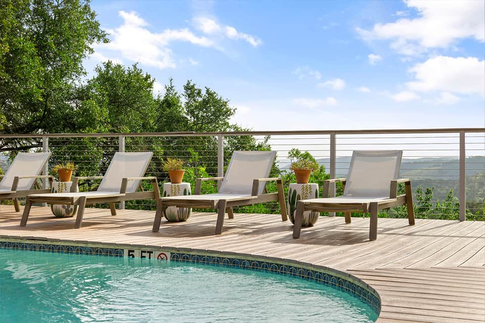 Elevated pool deck with loungers, metal railing, trees, and scenic valley views