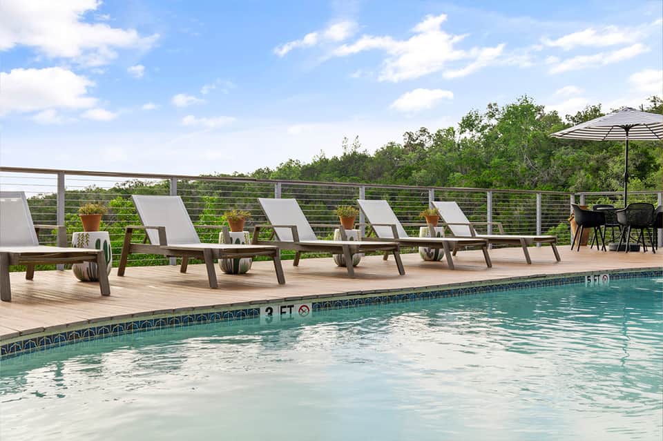 Resort pool deck with lounge chairs, striped umbrella, natural landscape views, and modern railings