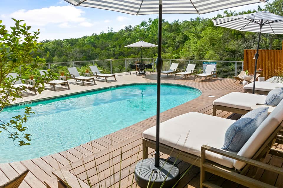 Resort pool with turquoise water, striped umbrellas, lounge chairs, and forest backdrop