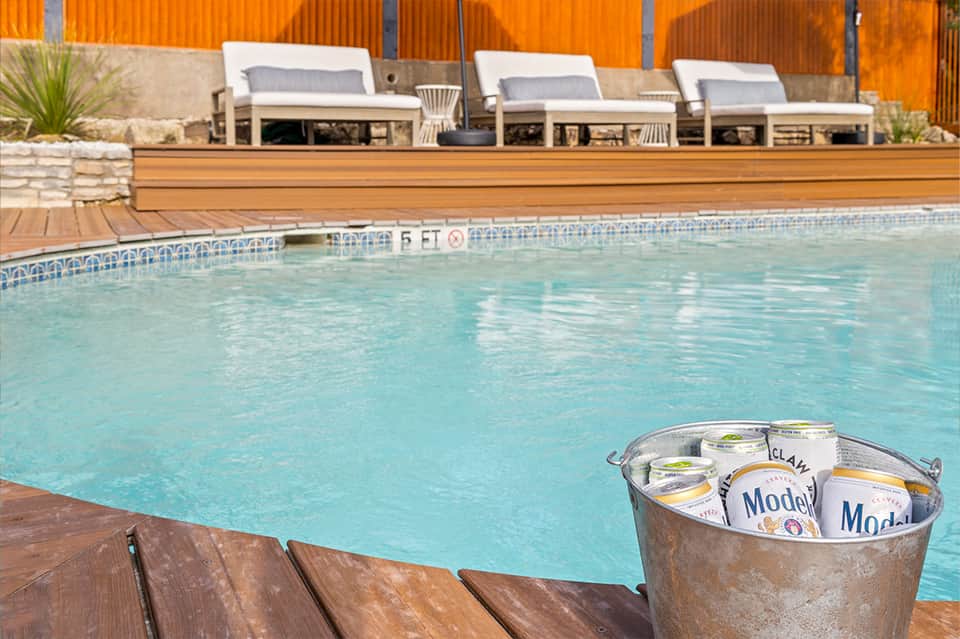 Pool with wooden deck, lounge chairs, and bucket of Model beer cans