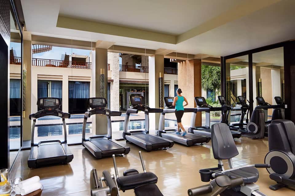 Modern fitness center with multiple treadmills, large windows overlooking courtyard and pool area