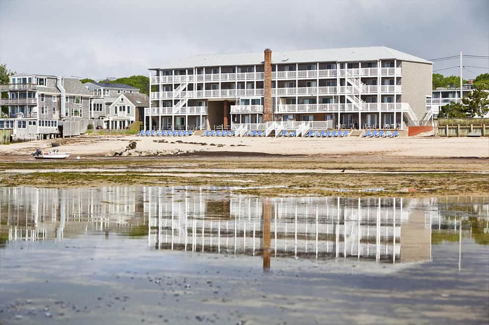 Beachfront hotel building with rows of blue loungers reflected in shallow water