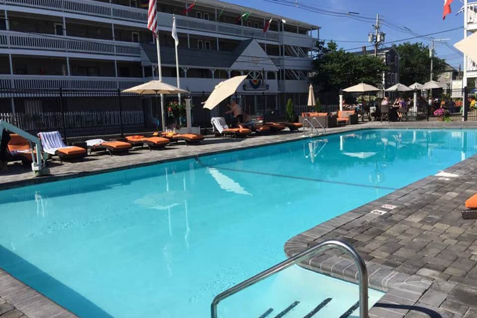 Outdoor swimming pool with lounge chairs, umbrellas, multi-story hotel building, and poolside seating