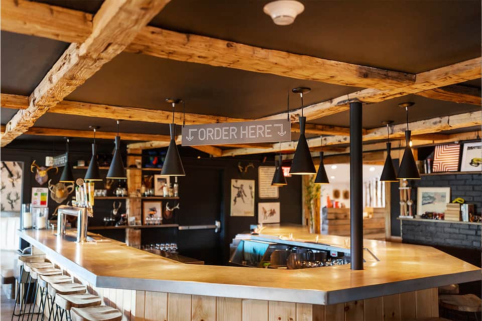 Rustic bar interior with exposed wooden beams, black pendant lights, and wooden countertop