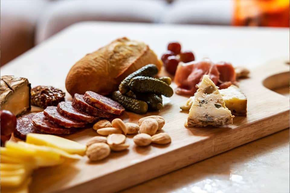 Charcuterie board with cured meats, cheeses, pickles, nuts, bread, and grapes on wooden serving platter
