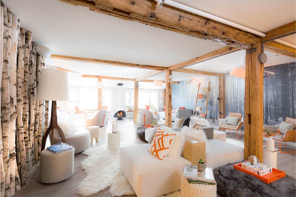 Modern lounge with exposed wooden beams, cream furniture, fireplace, orange accents, and floor-to-ceiling windows