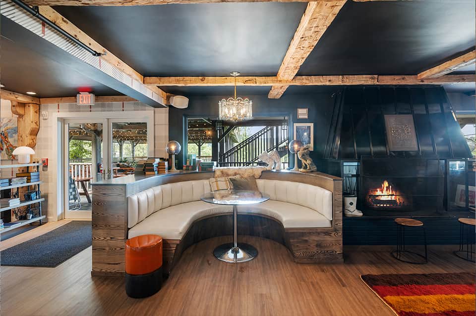 Modern lodge interior with curved cream seating, fireplace, exposed wood beams, and blue ceiling