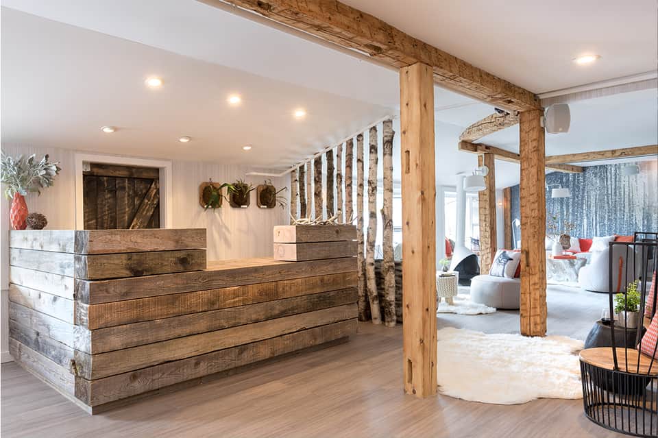 Rustic hotel lobby with wooden reception desk, exposed beams, and white railings separating seating area