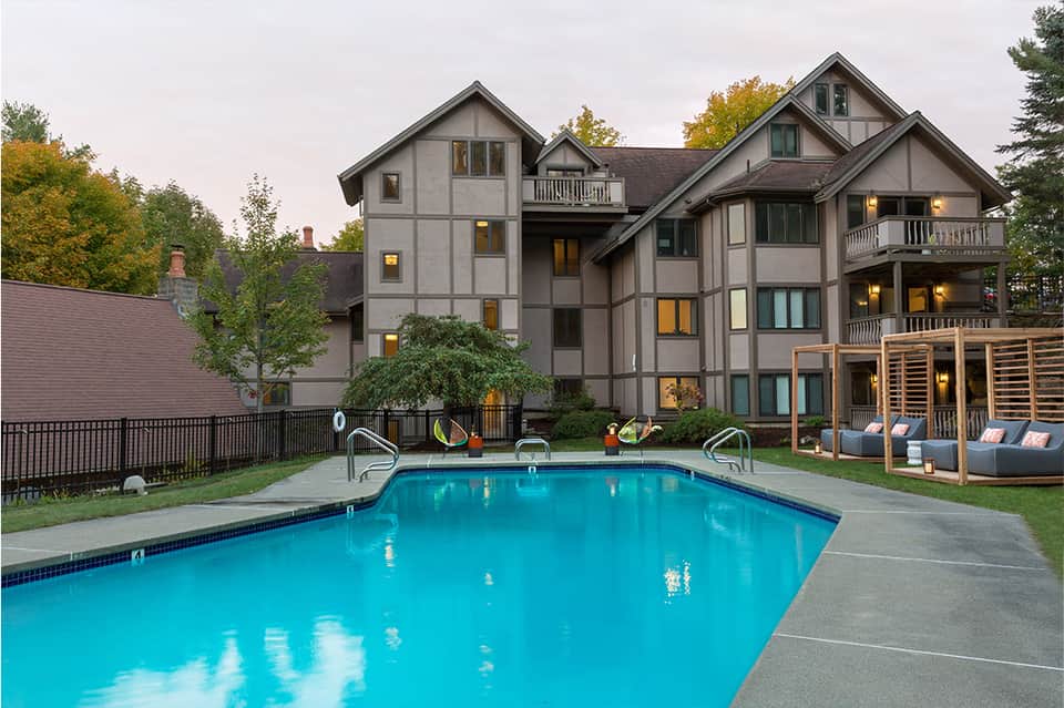 Modern Tudor-style residential building with pool, lounge chairs, and wooden pergola in autumn setting