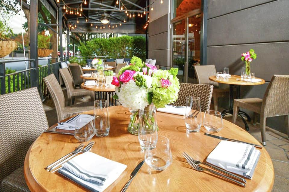 Upscale outdoor dining terrace with wooden tables, fresh floral centerpieces, and string lights