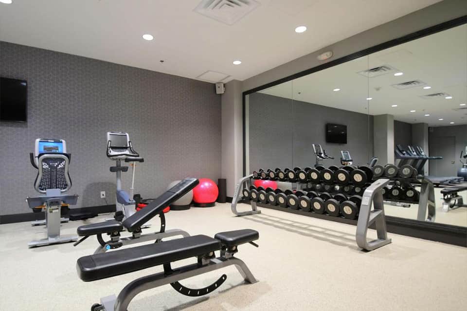 Fitness center with cardio equipment, free weights, dumbbells, and large mirror wall