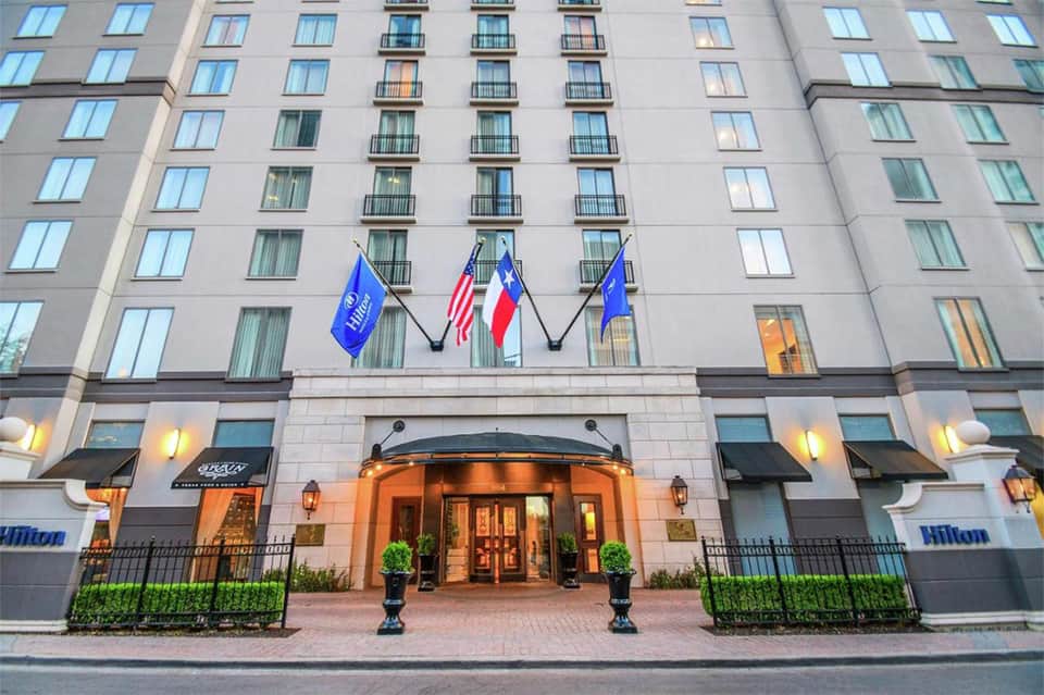 Hilton hotel entrance with elegant stone facade, flags, and manicured landscaping at dusk