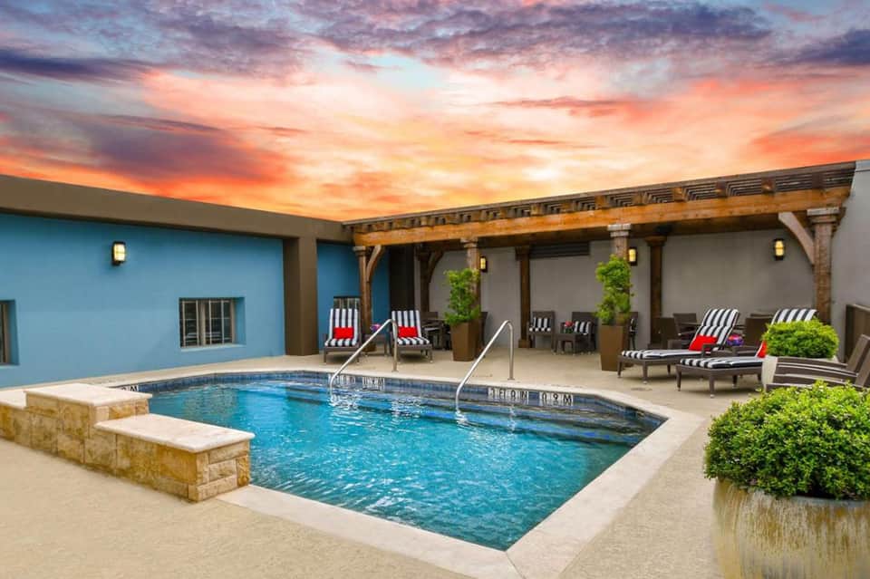 Indoor resort pool at sunset with lounge chairs, covered patio, and blue accent wall