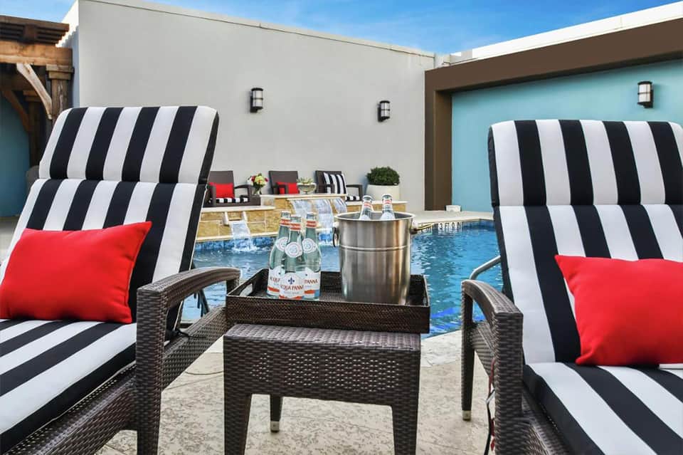 Poolside lounge area with striped black and white chaise lounges and red accent pillows
