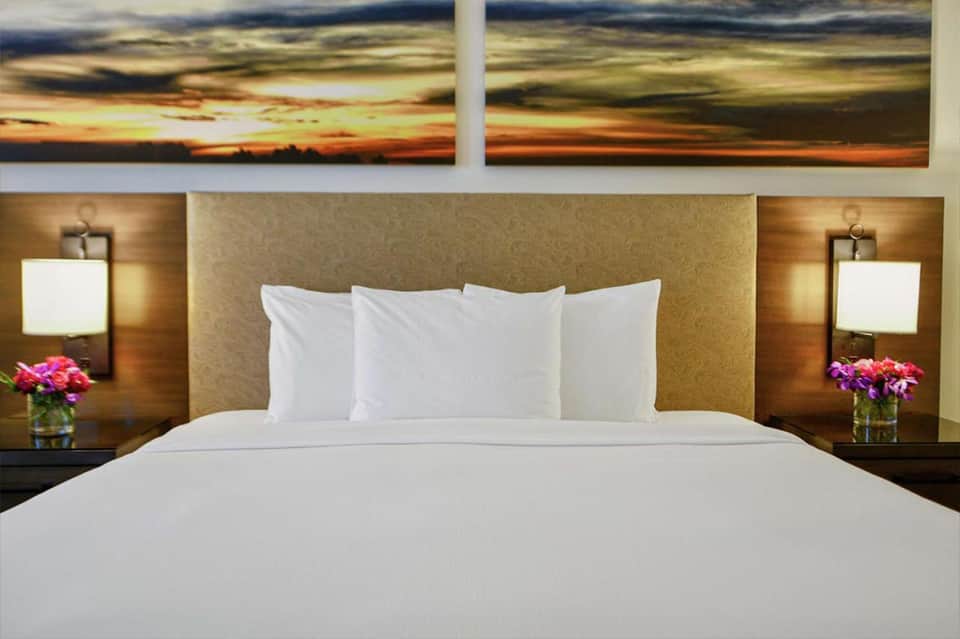 Hotel bedroom with queen bed, sunset artwork above headboard, and modern lighting