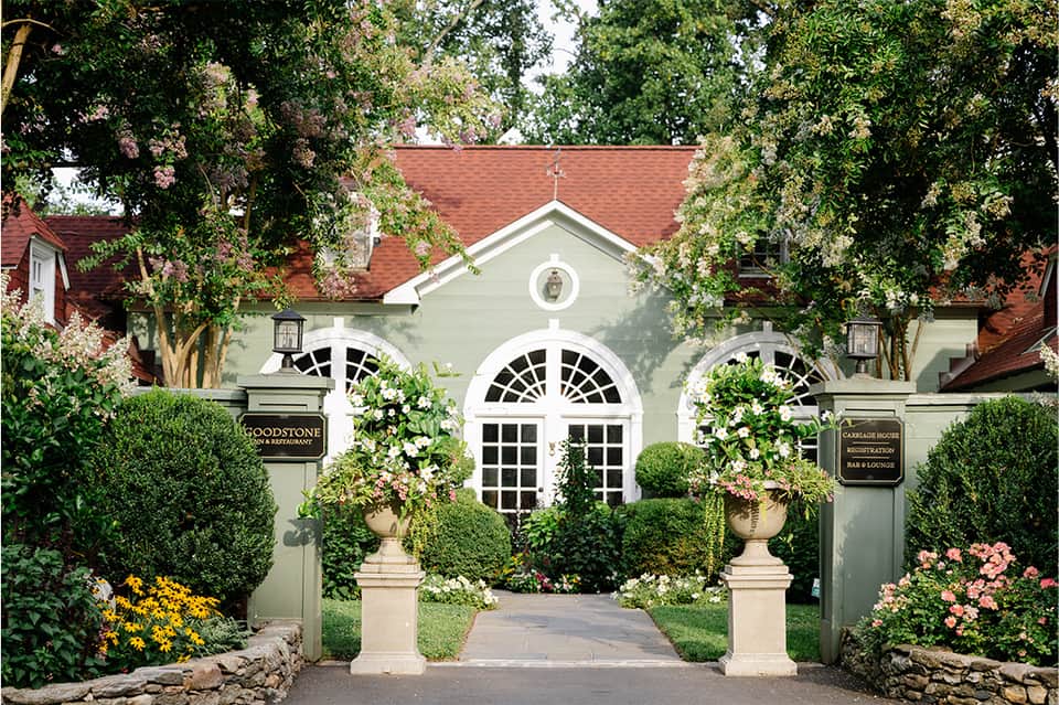 Elegant stone entrance to Goodstone Inn restaurant with arched windows, manicured hedges, and flowering planters