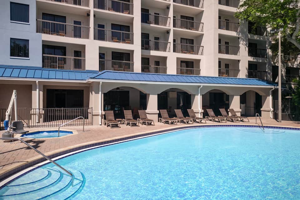 Hotel pool area with lounge chairs and blue metal awning covering outdoor seating beneath apartment balconies