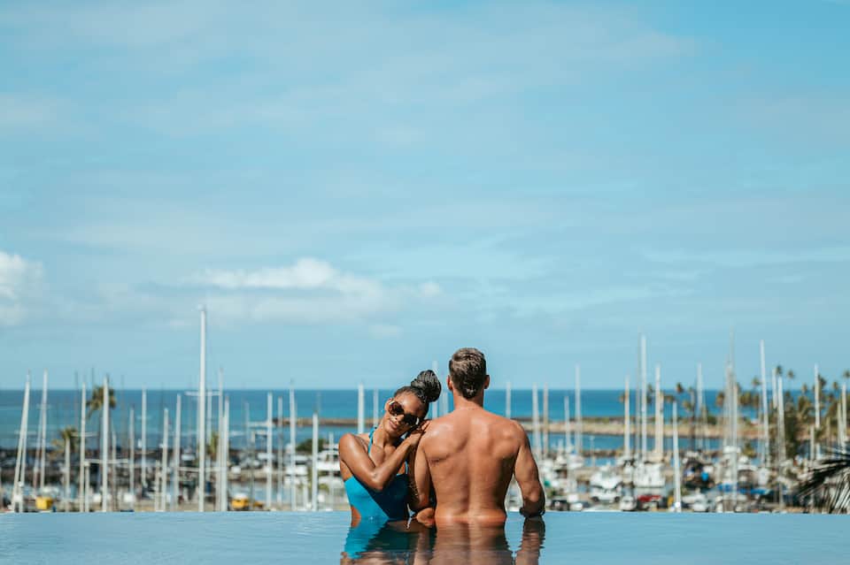 Couple relaxing in infinity pool overlooking marina with sailboats and palm trees