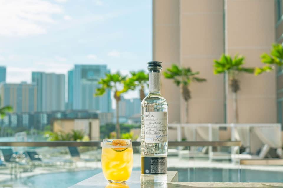 Cocktail with bottle on poolside table overlooking city skyline and palm trees