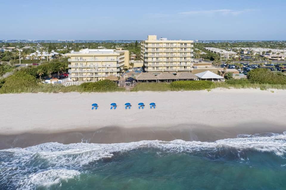 Oceanfront hotel buildings with blue umbrellas on sandy beach and crashing waves in foreground