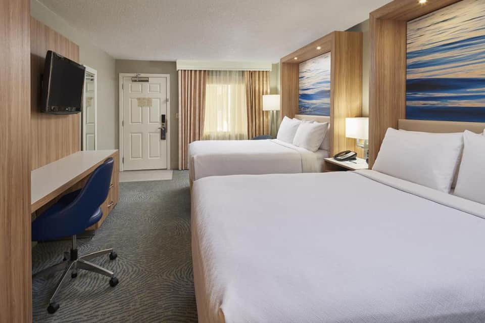 Modern hotel bedroom with two queen beds, wood accents, TV, and contemporary furnishings