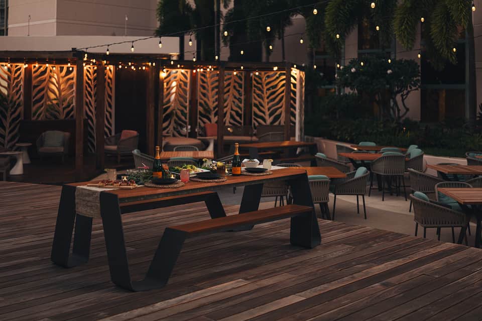 Evening patio dining setup with wooden tables, woven chairs, and decorative screens