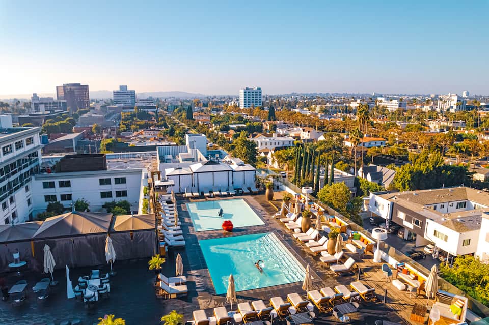 Aerial view of rooftop pool and lounging area overlooking a sprawling city landscape with mountains