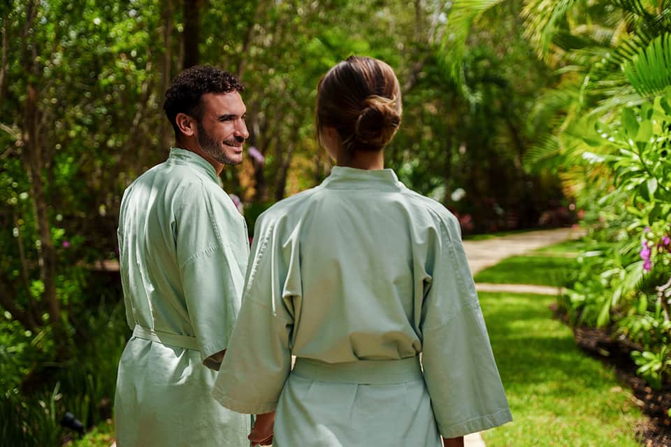 Couple in matching green robes walking through lush tropical garden with palm trees