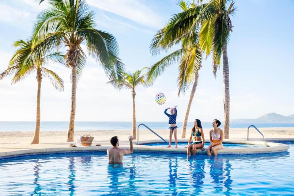 Family at beachfront pool under palm trees with ocean view and shallow water play area