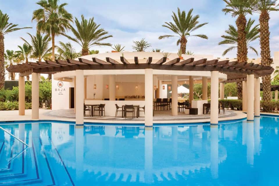 Resort pool pavilion with pergola, white columns, and palm trees under blue sky