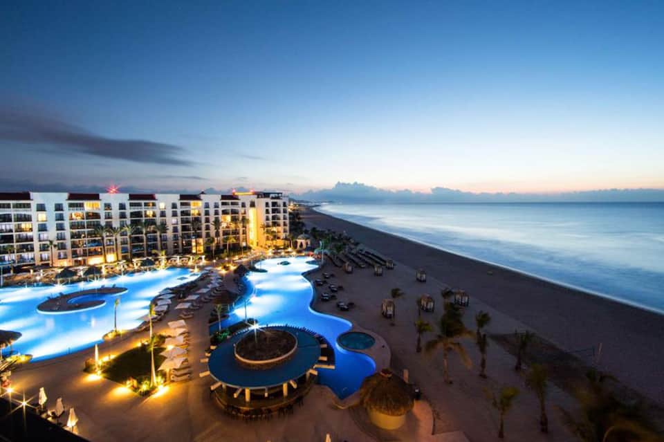 Beachfront resort at dusk with illuminated pools, palm trees, and ocean views