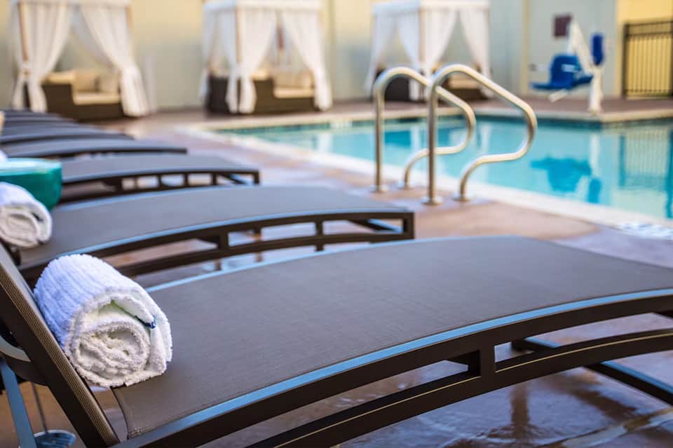 Indoor pool area with lounge chairs, rolled towels, pool railings, and cabana-style drapes
