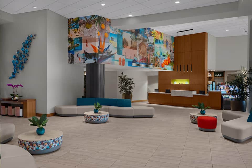 Modern hotel lobby with colorful wall art, curved seating, planted arrangements, and wooden reception desk
