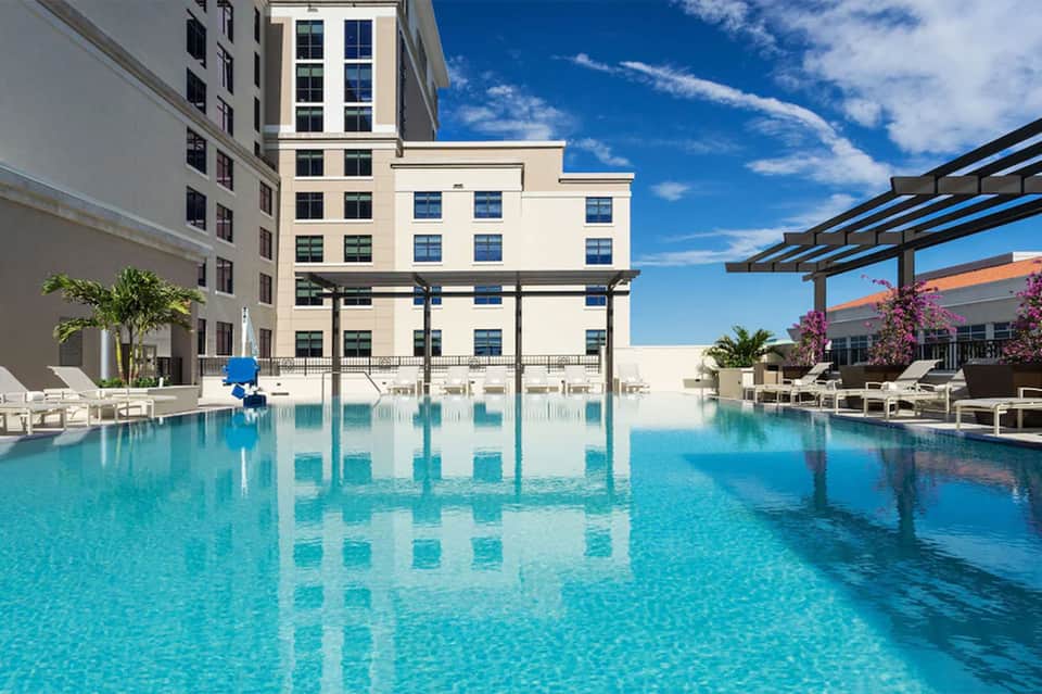 Crystal-clear turquoise pool with modern apartment buildings and pergola shade structures under blue sky