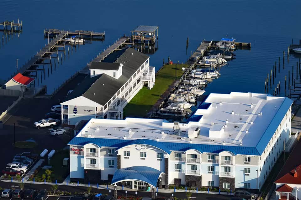 Aerial view of waterfront resort with white building, boat docks, and blue water