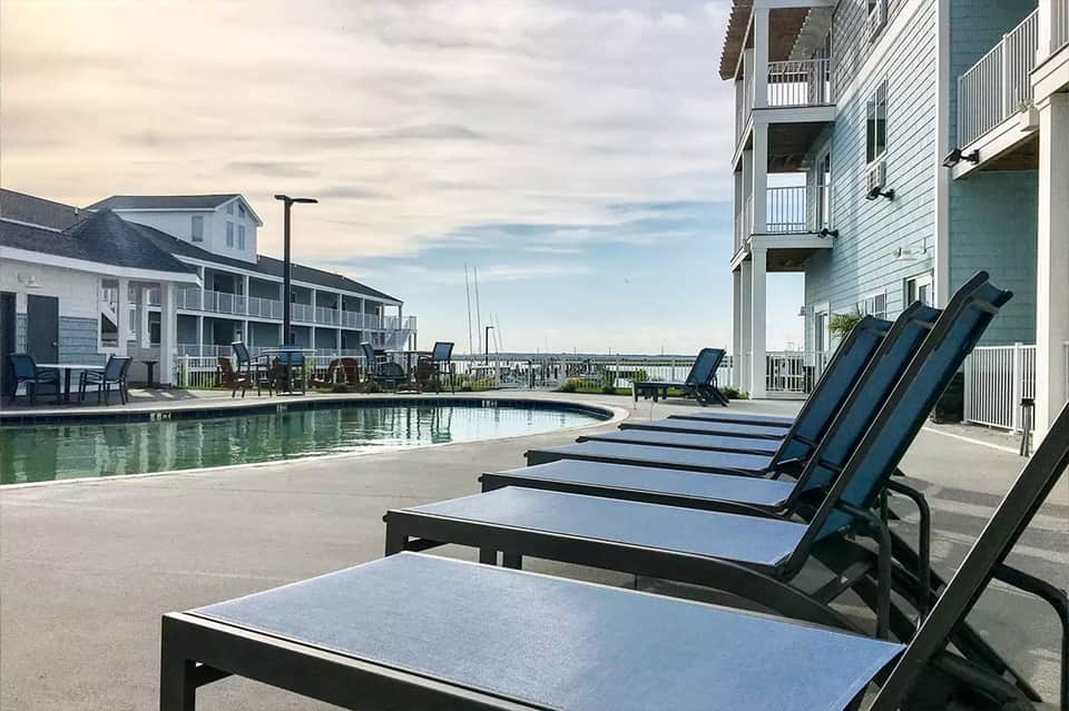 Waterfront resort pool with lounge chairs facing bay and sailboats