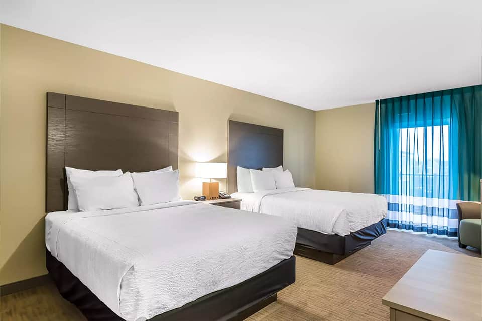 Hotel room with two queen beds, beige walls, turquoise curtains, and modern furnishings